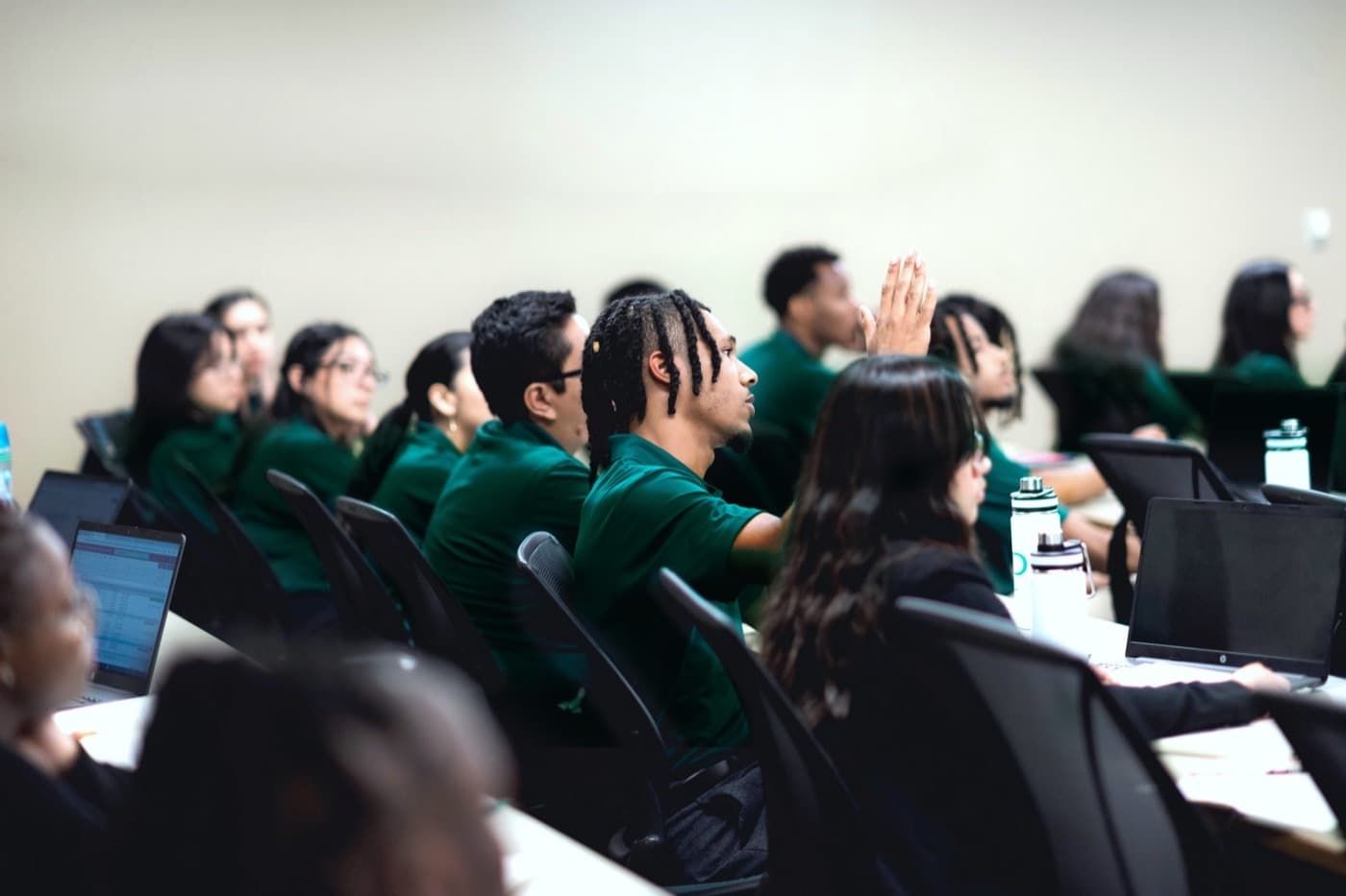 Greenwood Project Scholars at laptops during a training session, one raising a hand to ask a question.